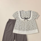 Close-up of lace trim and bow detail on girls' floral print top with grey pants