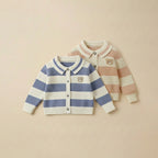 Two children's cardigans, one striped blue and white, the other striped pink and white, on a beige background.